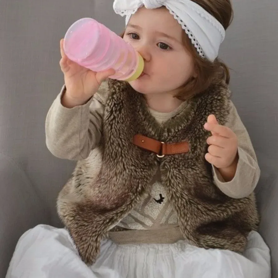 Une petite fille tenant seule son BIBEON rose et buvant